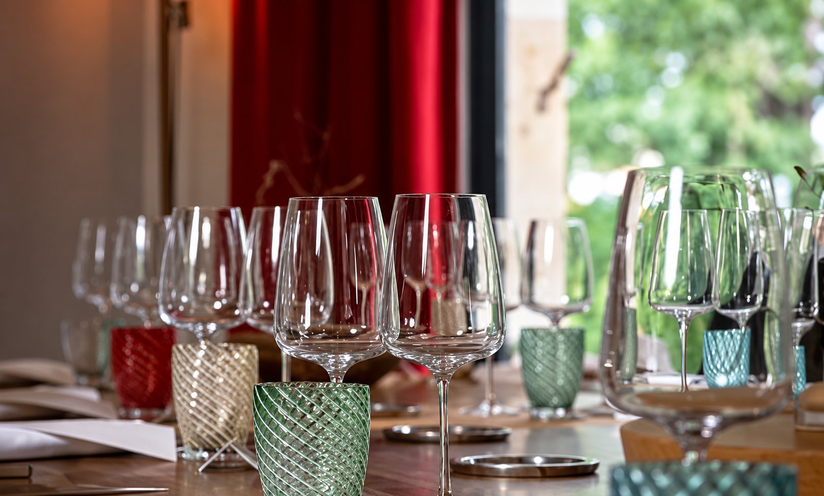 Verres à vin colorés sur une table dressée près d’une fenêtre
